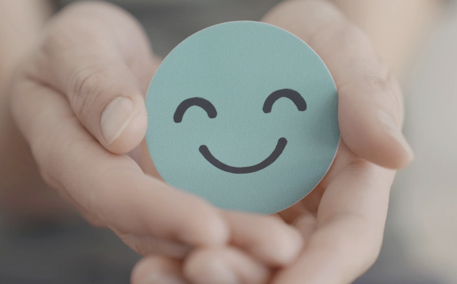 Cutout of a blue smiley face being held in a hand